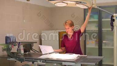 一位年轻的金发女护士在兽医诊所准备一张手术台，把灯伸直，放下下面的桌子。 旧的